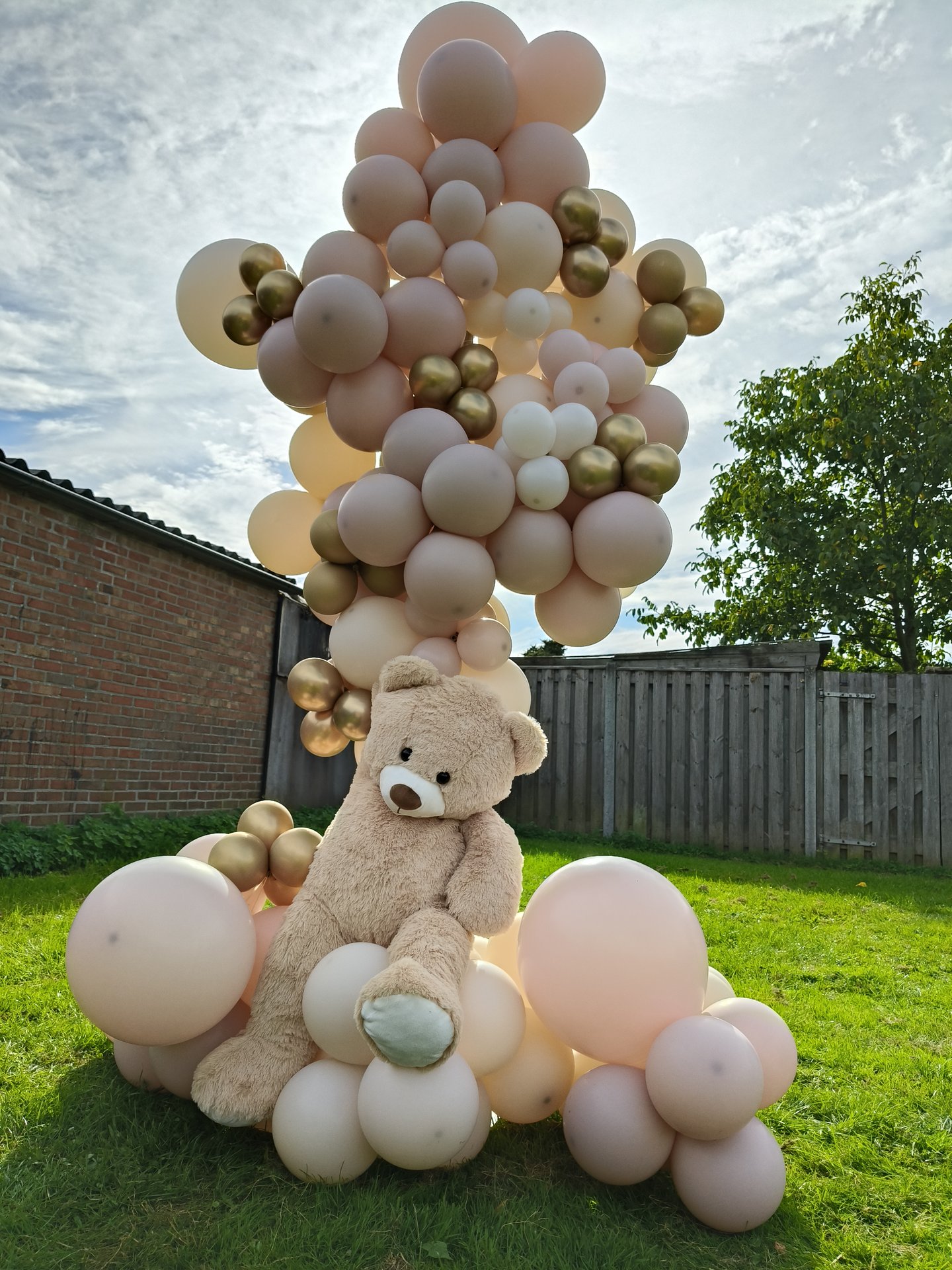 Organische ballonzuil in blush en goud met een grote teddybeer op het gras